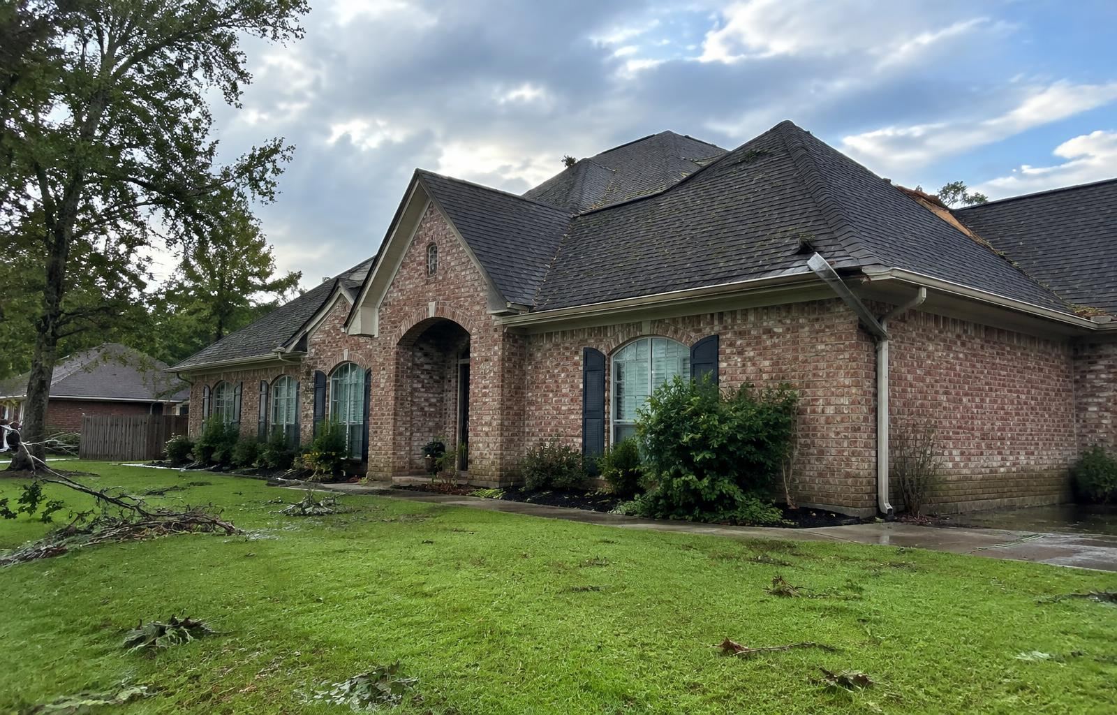 Brick home with storm debris on the lawn and a damaged gutter after a storm in Lafayette, Louisiana